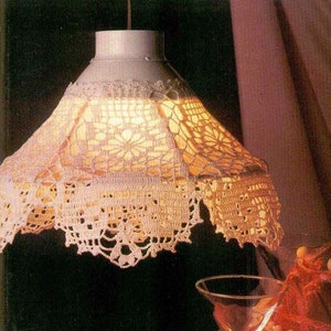 May include: A white crocheted lampshade with a delicate floral pattern hangs over a red tablecloth. A martini glass and a plate of red dessert are on the table.