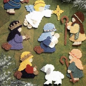 Puede incluir: Una colección de adornos navideños hechos a mano con figuras del pesebre. Los adornos incluyen ángeles, pastores, reyes magos y un cordero, todos elaborados con una apariencia texturizada y cosida. La paleta de colores incluye azul, dorado, blanco y marrón.