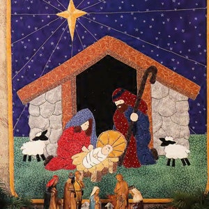 May include: A quilted Christmas nativity scene with a blue starry sky, a brown wooden stable, and a manger with a baby Jesus. There are three wise men, a shepherd, and two sheep. The scene is surrounded by pine branches.