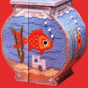 May include: A handmade, needlepoint fishbowl-shaped box. The box features a blue background with a red and orange goldfish, bubbles, and aquatic plants. The base is tan, and the box has a lid. The background is a light blue color.