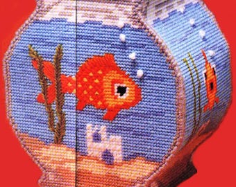 May include: A handmade, needlepoint fishbowl-shaped box. The box features a blue background with a red and orange goldfish, bubbles, and aquatic plants. The base is tan, and the box has a lid. The background is a light blue color.