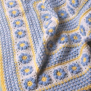 Pode incluir: Um cobertor de bebé em crochê com um padrão floral azul e branco e uma borda amarela.