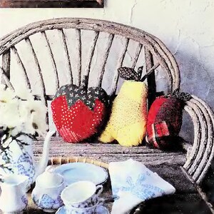 Puede incluir: Una silla de madera con un cojín de tela blanca con un patrón floral. Tres cojines de tela están en la silla, uno rojo, uno amarillo y uno rojo y blanco. Un juego de té con una tetera, un azucarero y dos tazas de té están en una bandeja de madera. Una servilleta de tela blanca está en la bandeja.