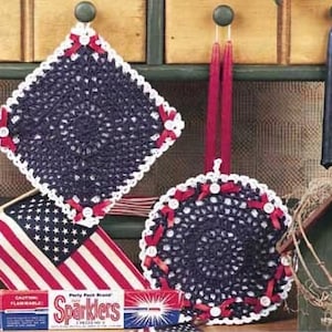 May include: Two crocheted doilies in red, white, and blue colors. The doilies are made with a delicate, lacy pattern. The doilies are hanging on a wooden shelf with a red, white, and blue American flag in the background.