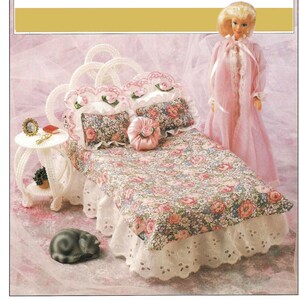 May include: A white doll bed with a floral patterned bedspread and a white lace ruffle. The bed has a white headboard with pink and white roses. There are two pillows with floral patterns and a pink pillow with a white rose. A small white table with a mirror and a book sits next to the bed. A gray cat is lying on the floor next to the bed.