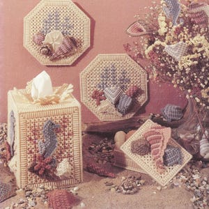 May include: A set of four crocheted items featuring a seashell and starfish theme. The set includes a tissue box cover, a small box, and two wall hangings. The items are all made in a beige yarn with blue, pink, and white accents.