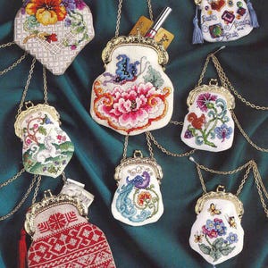 Puede incluir: Siete monederos bordados con cadenas y cierres dorados. Los monederos presentan varios diseños, incluyendo patrones florales, un pavo real, una mariposa y un patrón geométrico. Los monederos están colgados sobre un fondo de tela verde.