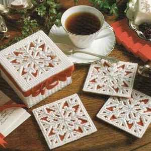 May include: Four white crocheted coasters with a snowflake design and red trim. A white crocheted box with a snowflake design and red ribbon is also shown.