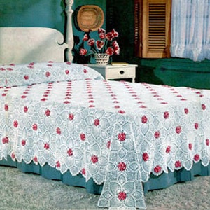 May include: A white crocheted bedspread with a delicate floral pattern and pink flower accents. The bedspread is on a bed with a white headboard and a blue bed skirt.