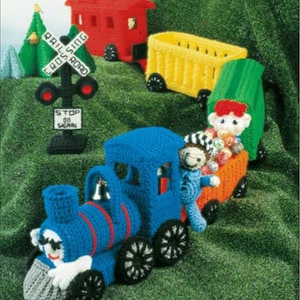 May include: A crocheted toy train set with a blue engine, a yellow boxcar, a green boxcar, and a red caboose. The train is on a green surface with a railroad crossing sign and a stop signal.