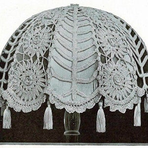 May include: A white crocheted lampshade with a floral design and tassels. The lampshade is made of delicate lace and has a scalloped edge.
