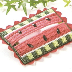May include: A handmade, rectangular tissue box cover in a watermelon design. The cover features red, green, and white yarn, with black seed accents. The edges are scalloped with a red trim, creating a fun, summery look.