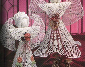 May include: Two crocheted angel ornaments with white lace and red flower accents. The angels are standing on a red velvet surface.