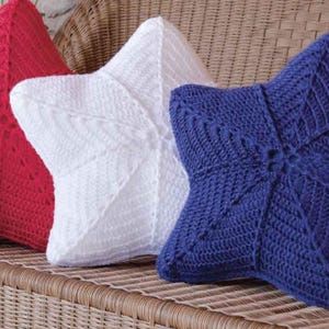 May include: Three crocheted star-shaped cushions in red, white, and blue. The cushions are arranged on a wicker sofa.