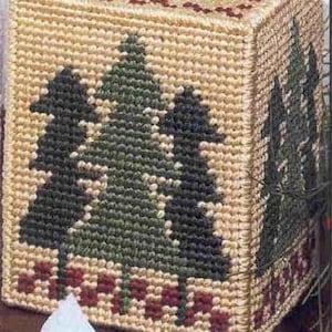 May include: A beige tissue box cover with a red and white border. The front of the cover features a cross-stitch design of three green pine trees.