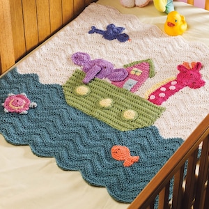 May include: A crocheted baby blanket with a blue, green, and white chevron pattern. The blanket features a crocheted ark with a giraffe, elephant, and bird on top. There is also a turtle and a fish on the blanket.