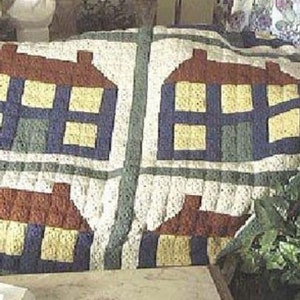 Puede incluir: Una manta de ganchillo con un patrón de casas. Las casas son en tonos de marrón, azul, amarillo y verde. La manta está hecha con hilo blanco y tiene un aspecto texturizado.