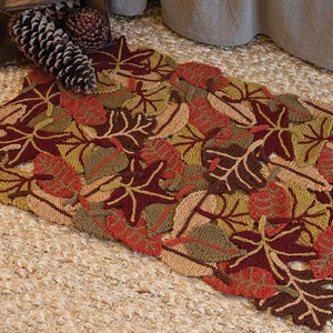 May include: A brown, green, and orange knitted rug with a leaf pattern. The rug is made of yarn and has a textured surface.