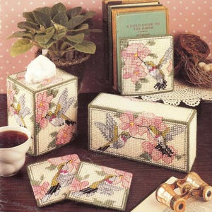 Op de afbeelding: Set van vier kruissteek-naaldvilt-knutselprojecten met kolibries en roze bloemen. De set bevat een tissuebox-hoes, een boekenlegger en twee onderzetters.