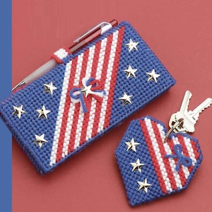 May include: A red, white, and blue fabric key chain in the shape of a heart with gold stars. The key chain is made of plastic canvas and has a red, white, and blue ribbon bow.