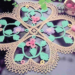 May include: A crocheted doily with a floral design in shades of pink, green, and yellow. The doily is made with a delicate lace pattern and has a scalloped edge.