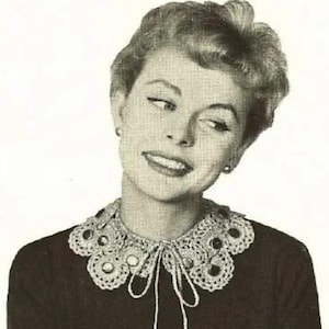 May include: A black and white photo of a woman wearing a crocheted collar with mirrored embellishments. The collar is tied at the neck with a bow.