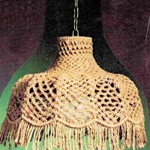 May include: A beige, handmade crochet lampshade with a fringed bottom edge. The lampshade is suspended from a chain and features an open weave design, allowing light to filter through. The overall aesthetic is rustic and bohemian.
