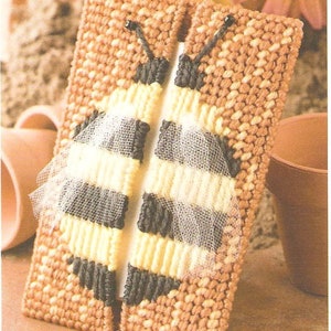 Puede incluir: Una funda para caja de pañuelos de tejido de punto marrón y amarillo con un diseño de abeja. La abeja tiene rayas blancas y negras y una superposición de malla translúcida.