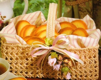 May include: A wicker basket filled with round, light brown cookies. The basket is decorated with a pink and white ribbon and a floral arrangement. The basket is sitting on a wooden table.
