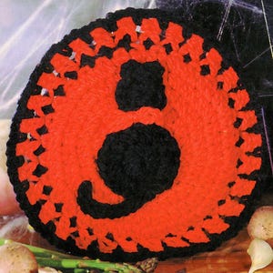May include: A crocheted black cat silhouette on a red background. The cat is surrounded by a black crocheted border.