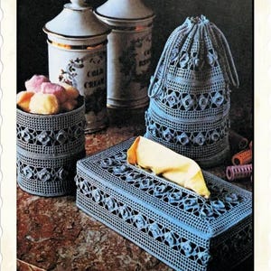 Puede incluir: Un conjunto de artículos de decoración para el hogar hechos a crochet en color azul. El conjunto incluye una tapa para caja de pañuelos, un pequeño contenedor cilíndrico y una bolsa de cordón. Todos los artículos están decorados con rosas de crochet.