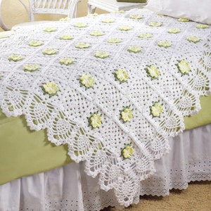 May include: White crochet throw blanket with a delicate floral pattern and yellow flowers. The blanket is draped over a bed with a white bed skirt.