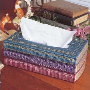 May include: A stack of three decorative tissue box covers in blue, purple, and red. Each box is rectangular and has a stitched design. White tissues are visible at the top of the blue box.