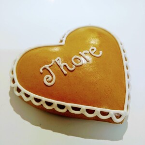 May include: A heart-shaped gingerbread biscuit decorated with white icing and the word "Th&ouml;re" written in cursive.