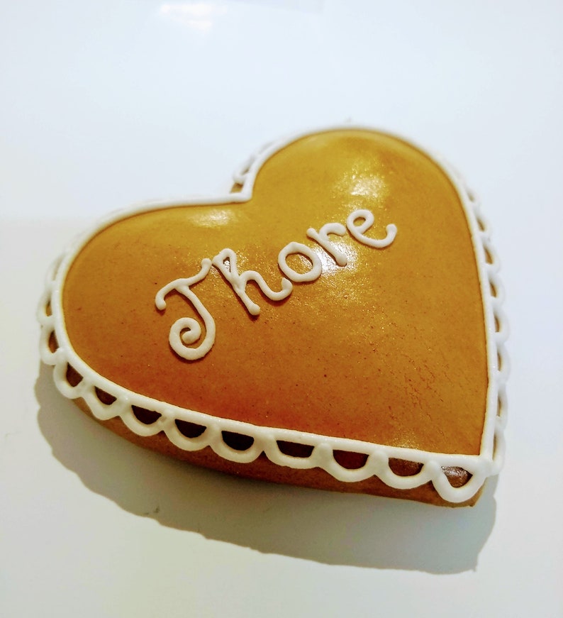 May include: A heart-shaped gingerbread biscuit decorated with white icing and the word "Th&ouml;re" written in cursive.