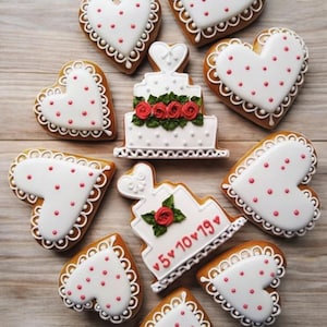 Puede incluir: Una variedad de galletas en forma de coraz&oacute;n y de pastel. Las galletas en forma de coraz&oacute;n tienen glaseado blanco con puntos rojos y bordes festoneados. Las galletas de pastel son blancas con rosas rojas y la fecha "5&bull;10&bull;19" en rojo.
