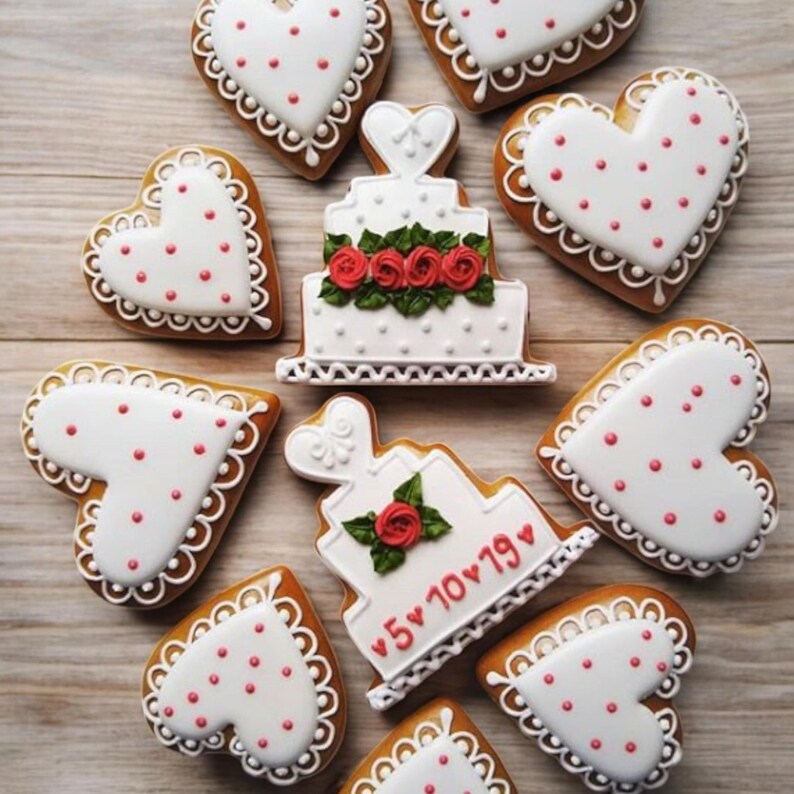 Puede incluir: Una variedad de galletas en forma de coraz&oacute;n y de pastel. Las galletas en forma de coraz&oacute;n tienen glaseado blanco con puntos rojos y bordes festoneados. Las galletas de pastel son blancas con rosas rojas y la fecha "5&bull;10&bull;19" en rojo.