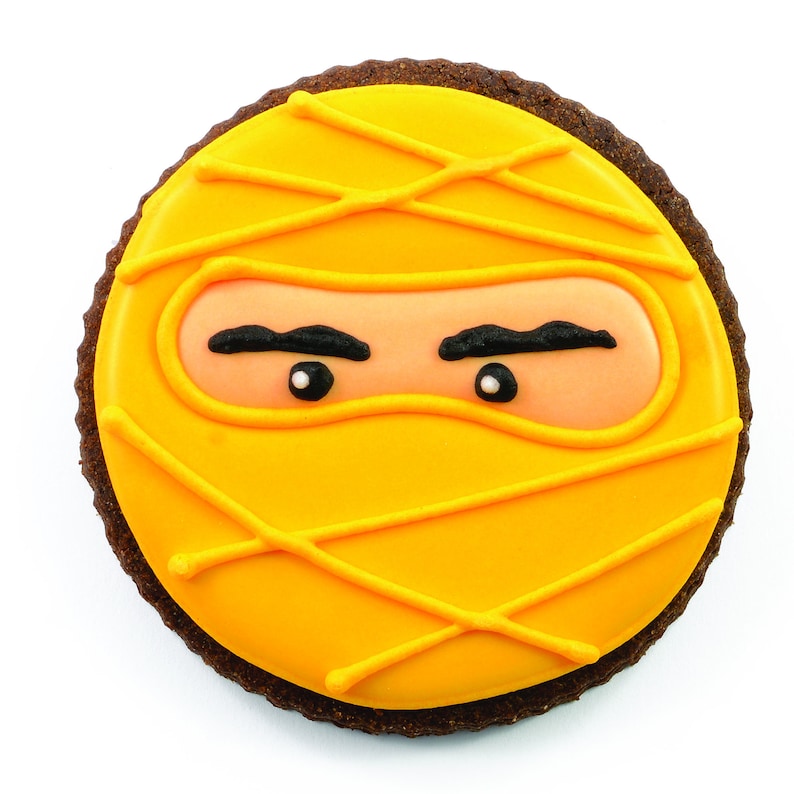 May include: A round chocolate cookie decorated with yellow icing and black icing details, resembling a ninja wearing a yellow mask.