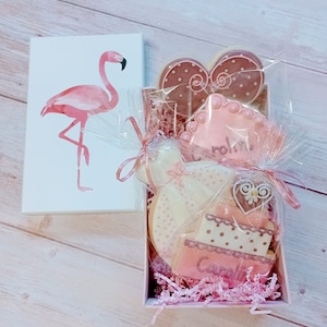 May include: A pink gift box containing pink and white cookies. The cookies are decorated with pink and white polka dots, hearts, and the names "Caroline" and "Robin".