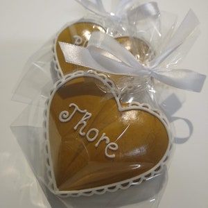 May include: Two heart-shaped gingerbread cookies, one with white icing and the word "Thorne" written on it, are wrapped in clear cellophane with white ribbons.