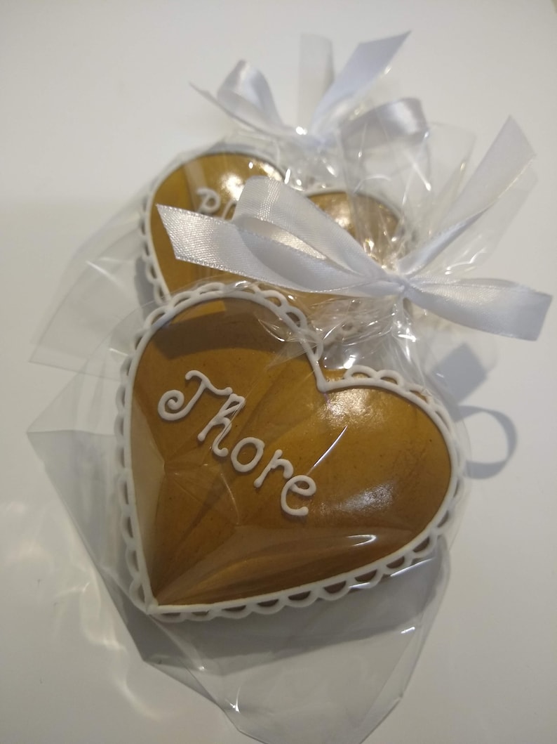 May include: Two heart-shaped gingerbread cookies, one with white icing and the word "Thorne" written on it, are wrapped in clear cellophane with white ribbons.