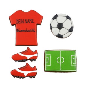 May include: A collection of soccer-themed cookies. Includes a red jersey with text, a soccer ball, a pair of red cleats, and a green field. The cookies are decorated with black and white icing.