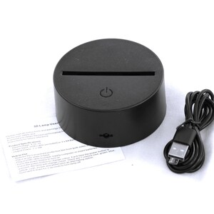 May include: A black 3D lamp base with a USB cable and instructions. The base has a power button and a slot for a 3D acrylic image. The instructions include product specifications and how to use the lamp.