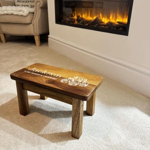 May include: A wooden step stool with a personalized inscription that reads "Jackson for Nanny & Grandad" and a tractor design. The stool is brown and has a natural wood finish.