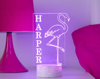 May include: A white acrylic night light with a pink flamingo silhouette and the name "HARPER" in white lettering. The light is on and emitting a purple glow.