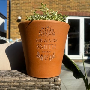 May include: Terracotta flower pot with a personalised inscription that reads "Mr. & Mrs. Smith 15.07.2024" with a heart and floral design.
