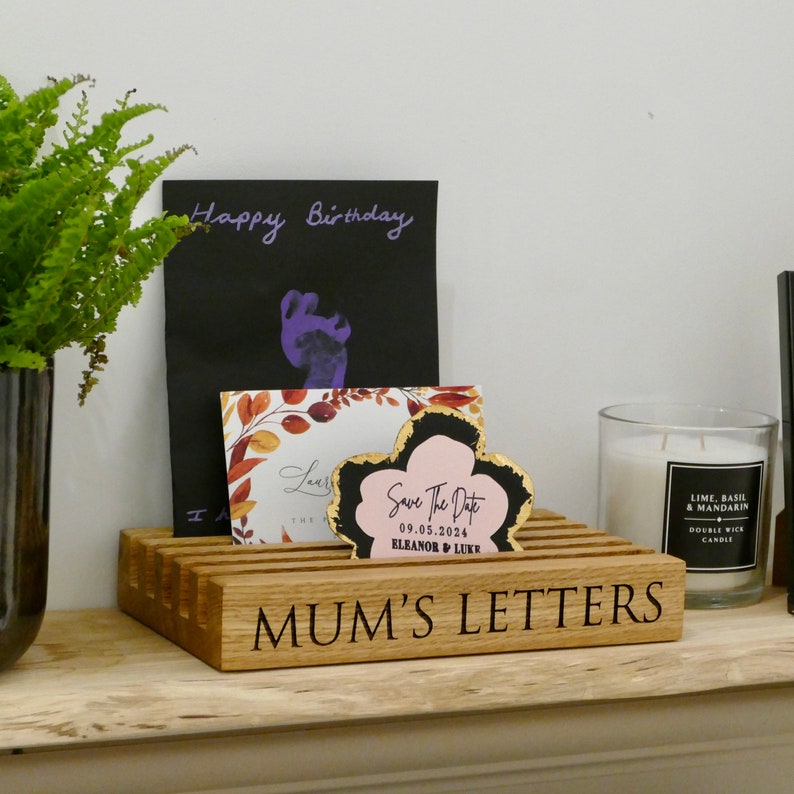 May include: A wooden letter holder with the text "MUM'S LETTERS" engraved on the front. The holder has slots for cards and envelopes. There are cards with the text "Happy Birthday" and "Save The Date 09.05.2024 ELEANOR & LUKE" on top of the holder.