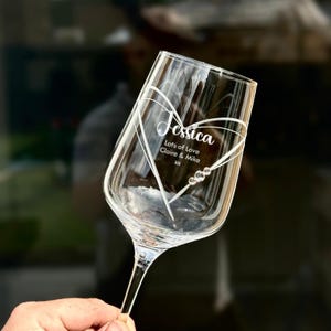 May include: A clear glass wine glass with a heart design etched into the side. The heart has the name "Jessica" and the text "Lots of Love Claire & Mike xx" inside.