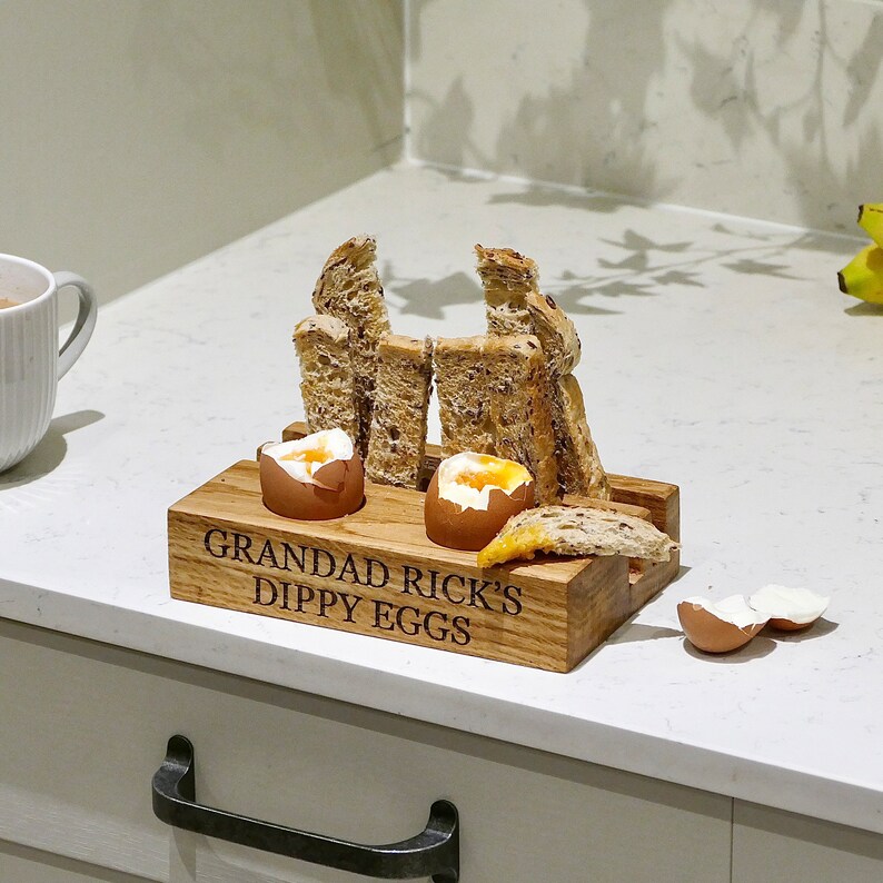 May include: Wooden egg holder with two eggs and toast. The holder is engraved with the text "Grandad Rick's Dippy Eggs".
