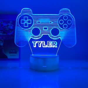 Könnte beinhalten: Ein blaues LED-Nachtlicht in Form eines Videospiel-Controllers mit dem Namen "TYLER" auf der Vorderseite.